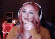 a woman wearing headphones and a yellow sweater is holding a microphone and smiling .