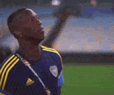 a man in a blue and yellow adidas shirt is standing on a soccer field looking up .