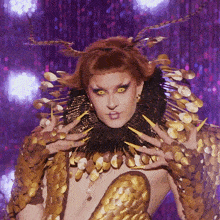 a drag queen is wearing a gold and black costume with feathers on her head