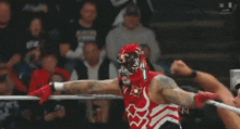 two men are wrestling in a ring and one of them is wearing a red shirt .