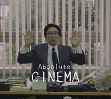 a man in a suit and tie is sitting at a desk with the words absolute cinema written on it
