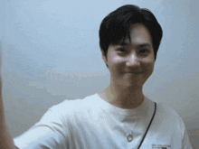 a young man wearing a white t-shirt with a necklace around his neck looks at the camera