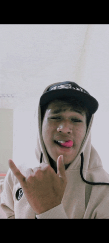 a young man wearing a hoodie and a hat sticks out his tongue