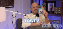 a man is sitting in front of a microphone holding a card that says tasty dark web .