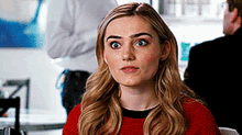 a woman in a red sweater is sitting at a table with a man in a white shirt behind her .