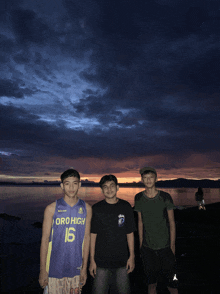 three young men standing in front of a body of water one of whom is wearing a jersey that says oro high 16