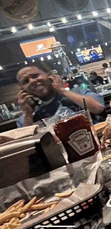 a bottle of ketchup sits on a table next to a man talking on a phone