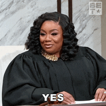 a woman in a judge 's robe is sitting at a table and says yes