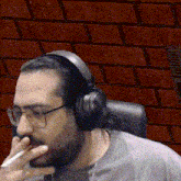 a man with glasses and headphones is smoking a cigarette in front of a brick wall