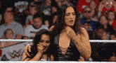 two women are standing next to each other in a wrestling ring with a crowd in the background .