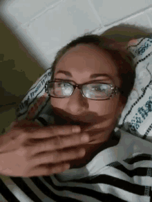 a woman wearing glasses is laying on a bed with her hand on her mouth