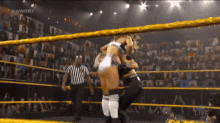 two women are wrestling in a wrestling ring with a referee in the background .