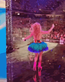 a woman in a colorful tutu is dancing on a stage in front of a crowd