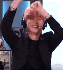 a man wearing headphones and a black jacket is holding his hands up in the air .