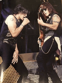 a man is singing into a microphone while another man plays a guitar on a stage .