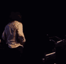 a man in a white shirt is playing a piano in the dark