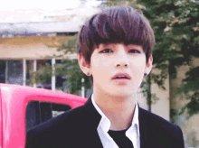 a young man wearing a black suit and tie is standing in front of a pink truck .
