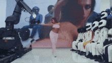 a woman in a pink outfit is dancing in front of a large screen