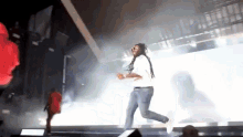 a man with dreadlocks is running on a stage while a woman in a red dress watches .
