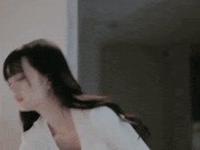 a woman in a white jacket is standing in a room with her eyes closed and her hair blowing in the wind .
