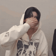 a man in a white hoodie is covering his face with his hand .