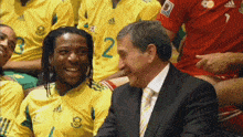 a man in a suit and tie talks to a man in a yellow adidas shirt