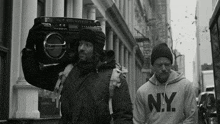 a man wearing a ny sweatshirt is carrying a boombox on his back