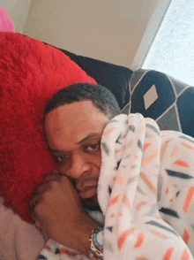 a man is laying on a couch with a blanket and a red pillow