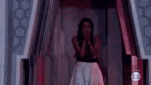 a woman in a white dress is standing in a room with her hands on her face .