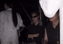 a man wearing sunglasses and a white shirt stands in the dark