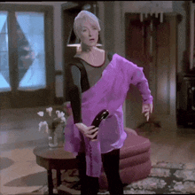 a woman wearing a purple shirt is holding a hair dryer