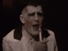 a man in a white suit is singing into a microphone in a dark room
