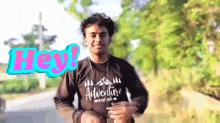 a young man wearing a black shirt that says adventure is standing in front of trees .