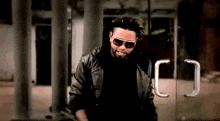 a man wearing sunglasses and a black leather jacket is standing in front of a glass door .