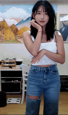 a woman in a white tank top and ripped jeans is standing in front of a painting