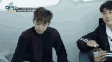 two young men are sitting next to each other and one is holding a bottle of something