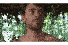 a shirtless man with a beard looks at the camera with trees in the background
