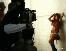 a woman is leaning against a wall while being filmed by a cameraman
