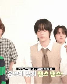 a man in a vest and tie is standing next to two other men with korean writing on their shirts