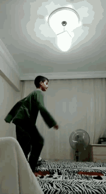 a boy in a green shirt is jumping in a bedroom