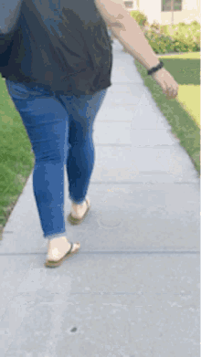 a woman is walking down a sidewalk wearing flip flops and jeans