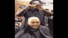 a man is getting his hair cut by a barber while wearing a cape that says fugitive .