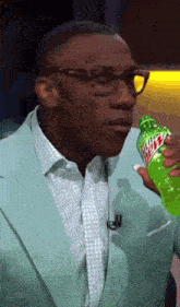 a man in a suit and glasses is drinking a bottle of mountain dew
