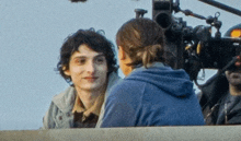 a man and a woman are sitting in front of a camera . the man is wearing a blue hoodie .