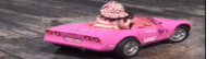 a woman is driving a pink car with a hat on .
