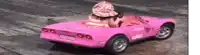 a woman is driving a pink car with a hat on .