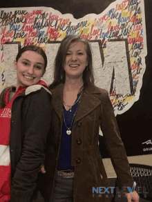 two women standing in front of a wall that says next level