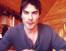 a man in a gray shirt is sitting in front of a wooden wall