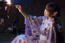 a woman in a purple floral kimono is holding a sparkler in her hand