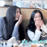 two girls are laughing and covering their mouths with their hands in a restaurant